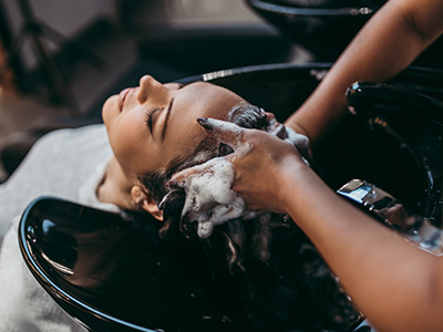 A hair salon scene with a person receiving a hair wash, featuring a stylist washing hair in a black basin.