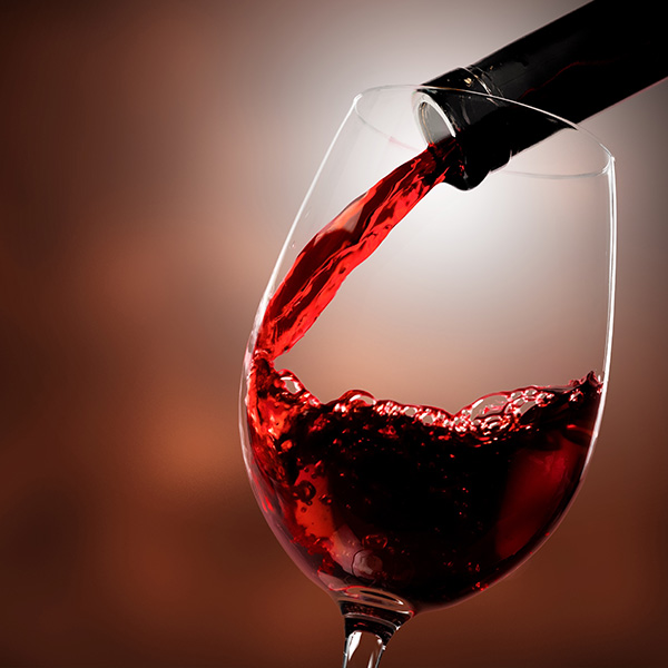 Alt text  Wine glass filled with red wine, with a single drop falling into it.